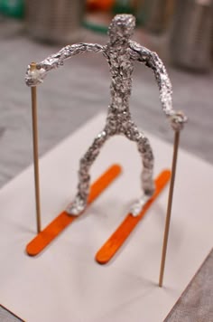 a sculpture of a man on skis made out of silver foil and orange sticks