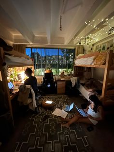 two people sitting on the floor in a dorm room with bunk beds and laptops