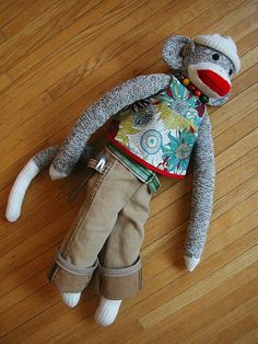 a sock monkey wearing a sweater and pants on the floor with wood floors in the background
