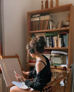 a woman sitting in a chair writing on a piece of paper with an easel next to her