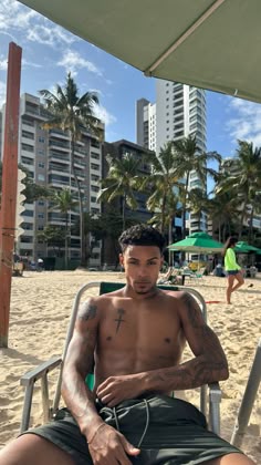 a shirtless man sitting in a chair on the beach with his arm around him