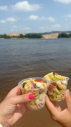 two people holding up plastic containers filled with pasta and veggies near the water
