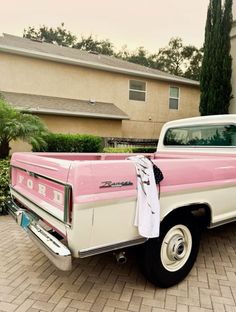 a pink and white truck parked on top of a brick driveway next to a house
