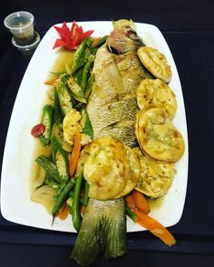 a white plate topped with fish and veggies on top of a black table
