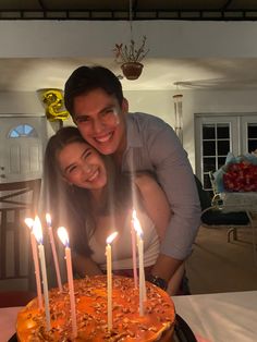 a man and woman are smiling in front of a cake with lit candles on it