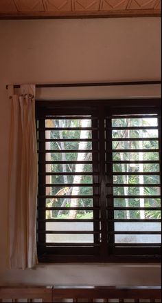 an open window with wooden blinds in front of it and trees outside the windowsill