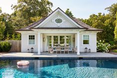 a pool house with an outdoor dining area next to it and a swimming pool in the foreground