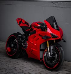 a red and black motorcycle parked next to a gray wall on a brick floored area