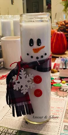 a candle with a snowman on it sitting on top of a table next to candles