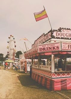 an old photo of a carnival booth with flags flying in the wind and people walking around