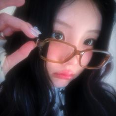 a woman wearing glasses with her hands on the side of her face and looking at the camera