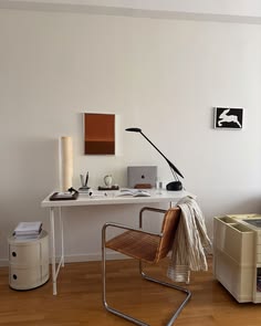 a desk with a chair, computer and other items on it in a white room