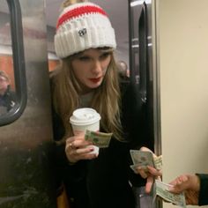 a woman in a hat is holding money and looking at her cell phone while riding the subway