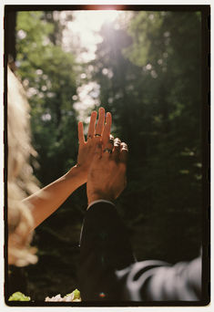 two people holding their hands up to each other in front of some trees and bushes