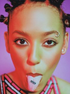 a woman with piercings on her nose and tongue sticking out to the side, in front of a purple background