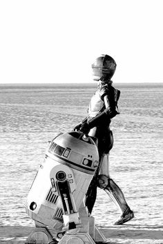 a robot walking across a sandy beach next to a person