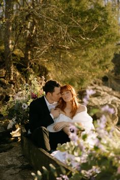 a bride and groom are sitting on a bench in the woods with wildflowers