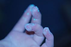 a person's hand with white and blue glitters on their fingers, holding something in the air