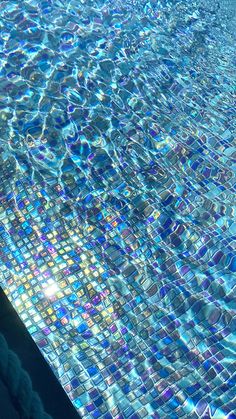 an empty swimming pool with blue water and sun reflecting off the glass tiles on it