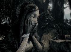 a woman with her hands on her face sitting in front of a tree and rocks