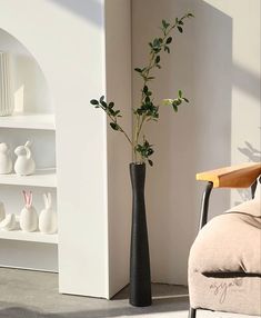 a tall vase with flowers in it sitting on the floor next to a chair and bookshelf
