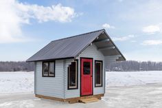 a small white house with a red door in the middle of a snowy field,