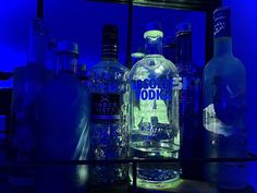 several bottles and glasses are sitting on a shelf in front of a blue lit background
