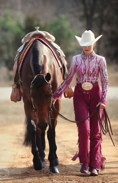 a woman leading a horse down a dirt road