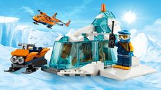 two legos are in the snow with an orange helicopter flying over them and one is on top of a building