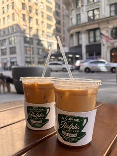 two cups of iced coffee sitting on top of a wooden table next to each other