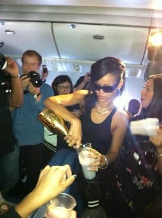 a group of people on an airplane with drinks in their hands and one woman pouring champagne into the glass