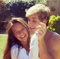 a young man and woman sitting on the grass together, one is smiling at the camera
