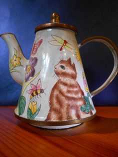 a teapot with a cat painted on it sitting on top of a wooden table