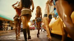 four women in short shorts and high heeled sandals are walking towards a yellow car