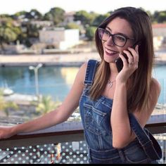 a woman in overalls talking on a cell phone while standing next to a railing