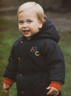a young boy in a black jacket is standing on the grass and smiling at the camera