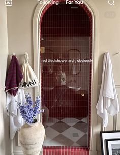 a bathroom with a red tiled shower and white towels hanging on the wall next to it