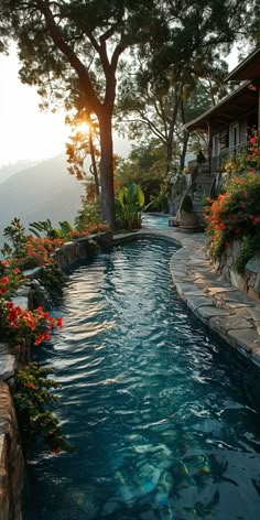an outdoor swimming pool surrounded by flowers and trees with the sun setting in the background