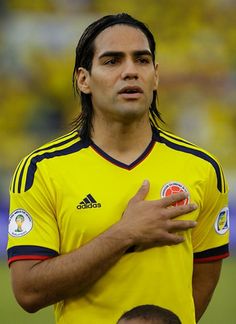 a soccer player with long hair standing in front of another player wearing a yellow shirt