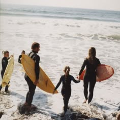 four people in wetsuits carrying surfboards into the ocean