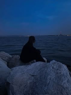 a person sitting on top of a rock next to the ocean at night with a full moon in the sky