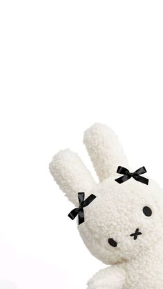 a white stuffed animal with a black bow on its head and ears sitting in front of a white background