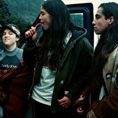 three people standing next to each other near a bus and one is brushing her teeth