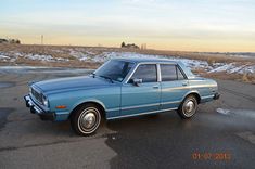 a blue car parked on the side of a road in front of snow covered ground