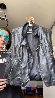 a man holding up a leather jacket in front of his face and eye patches on it