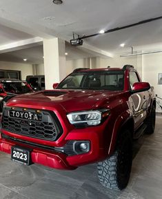 a red toyota truck is parked in a showroom with other trucks behind it and on the floor