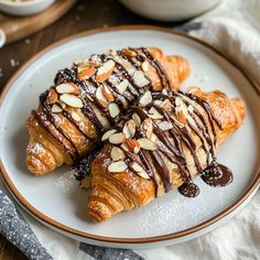 two croissants covered in chocolate drizzled with almonds on a plate