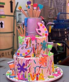 a multi - tiered birthday cake decorated with paint splatters and pencils