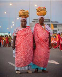 two women dressed in red and gold standing next to each other on the street with people behind them