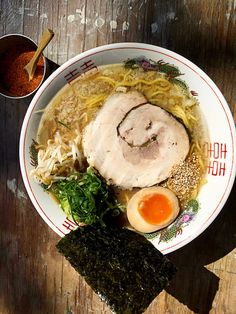 a bowl filled with noodles, meat and vegetables next to an egg on top of a wooden table